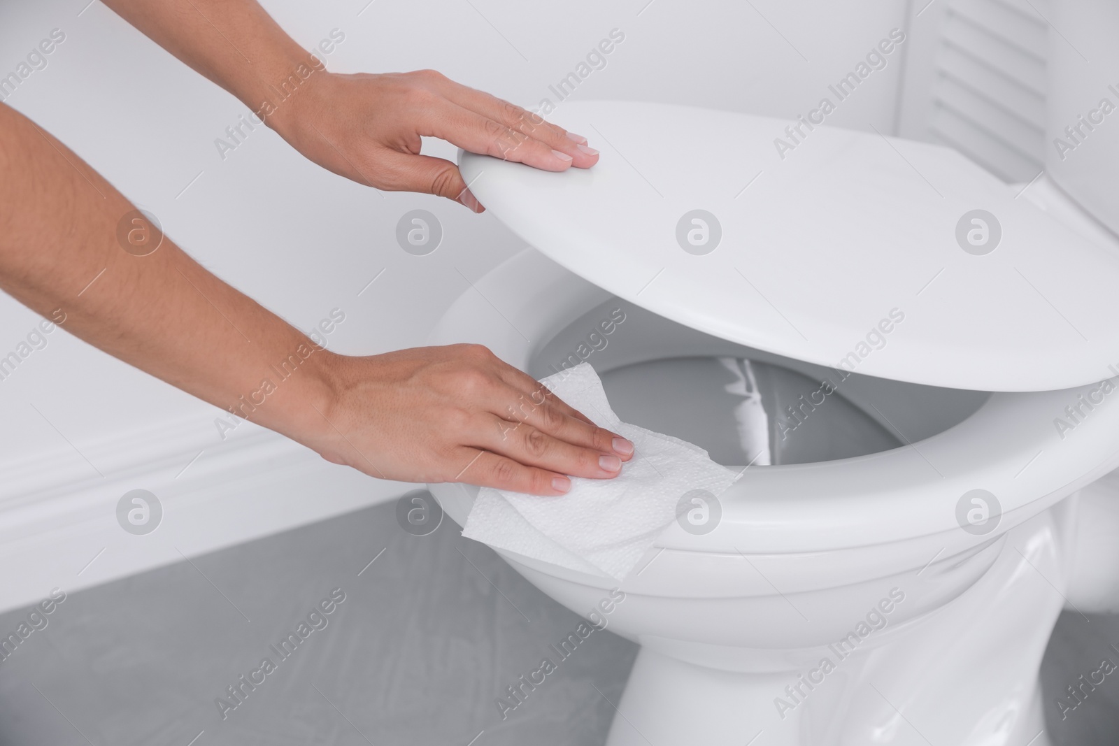 Photo of Woman wiping toilet seat with paper in bathroom, closeup