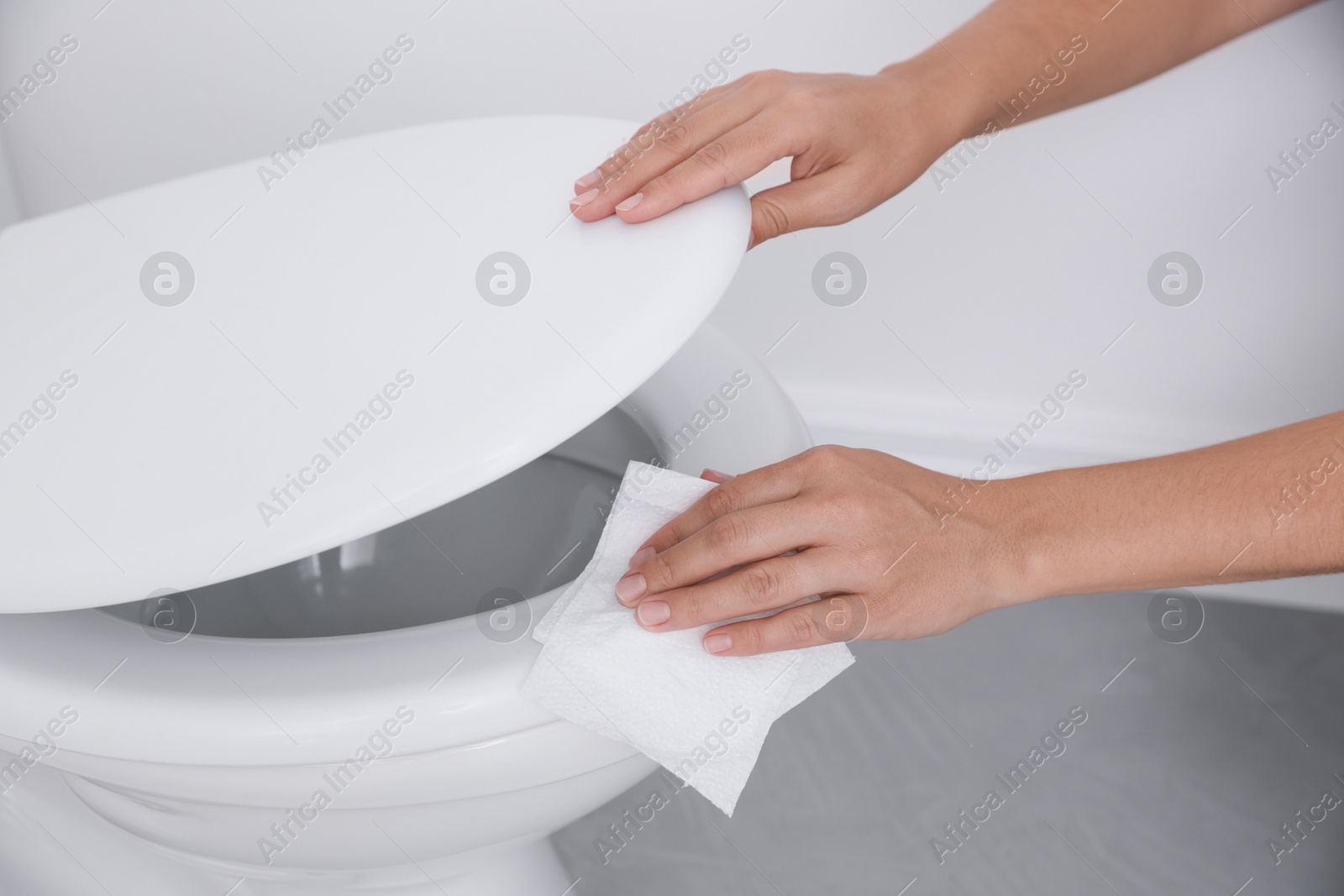 Photo of Woman wiping toilet seat with paper in bathroom, closeup