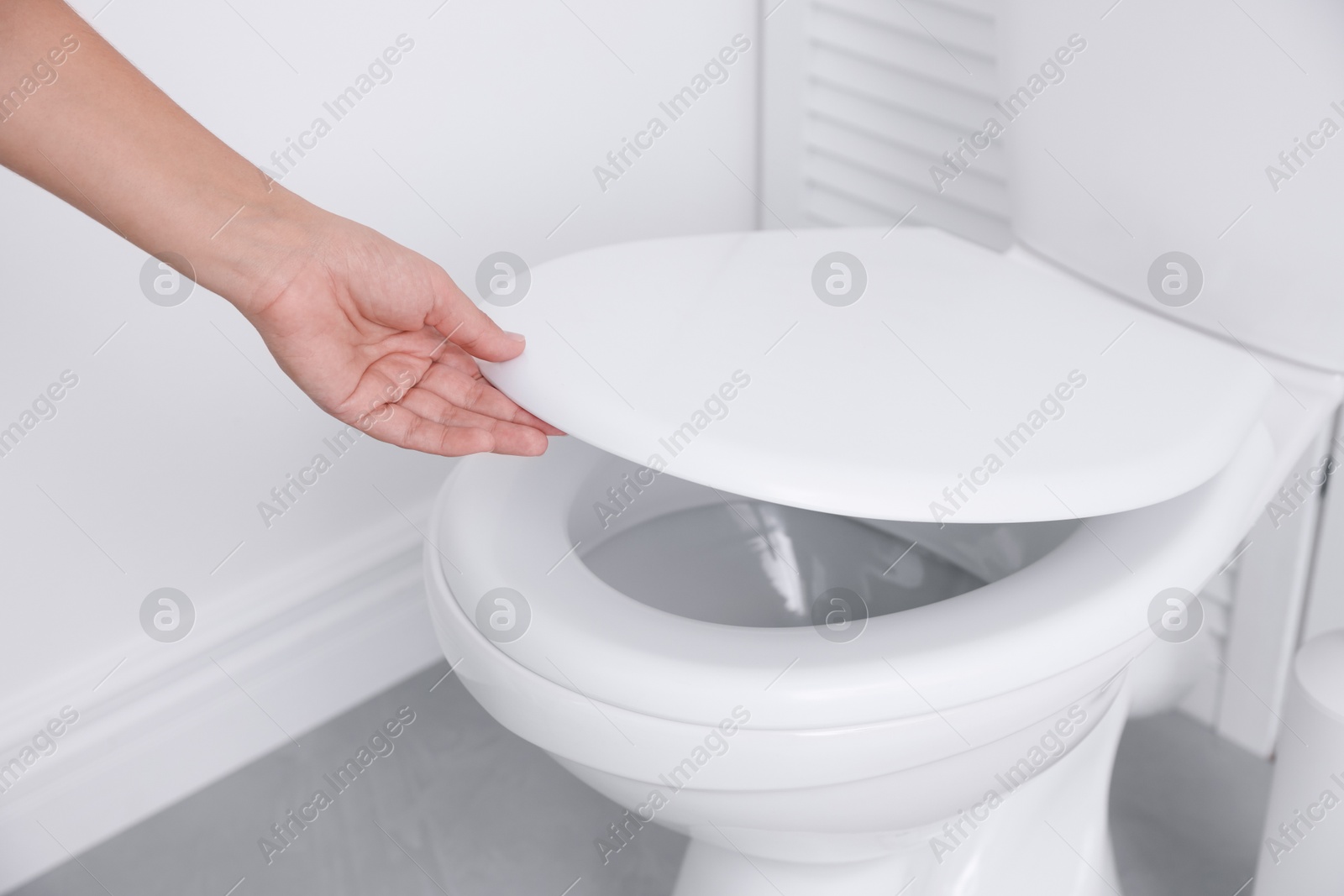 Photo of Woman closing toilet seat in bathroom, closeup