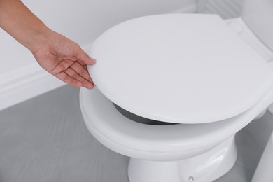 Photo of Woman closing toilet seat in bathroom, closeup