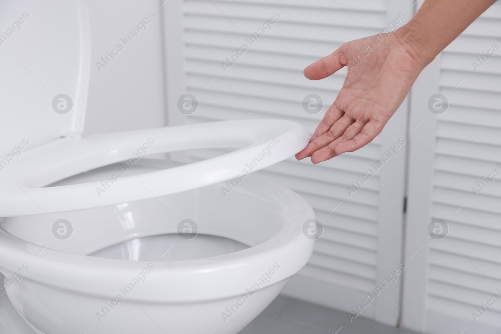 Photo of Woman closing toilet seat in bathroom, closeup