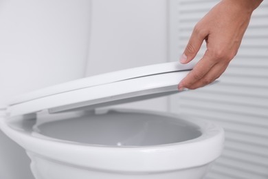 Photo of Woman closing toilet seat in bathroom, closeup