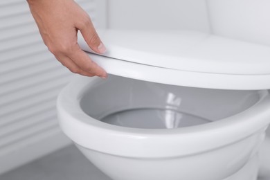 Photo of Woman closing toilet seat in bathroom, closeup