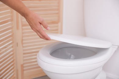 Photo of Woman closing toilet seat in bathroom, closeup