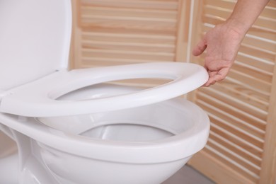 Photo of Woman closing toilet seat in bathroom, closeup