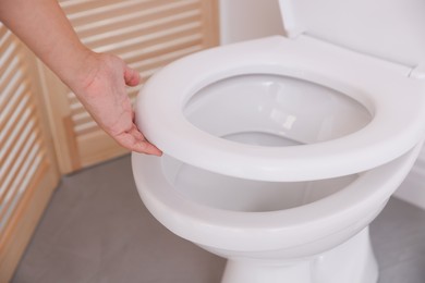 Photo of Woman closing toilet seat in bathroom, closeup