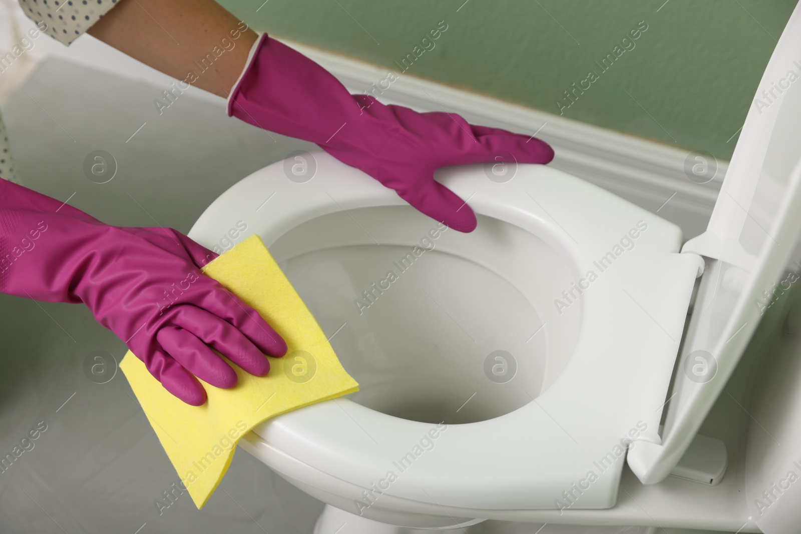 Photo of Woman cleaning toilet seat in restroom, closeup