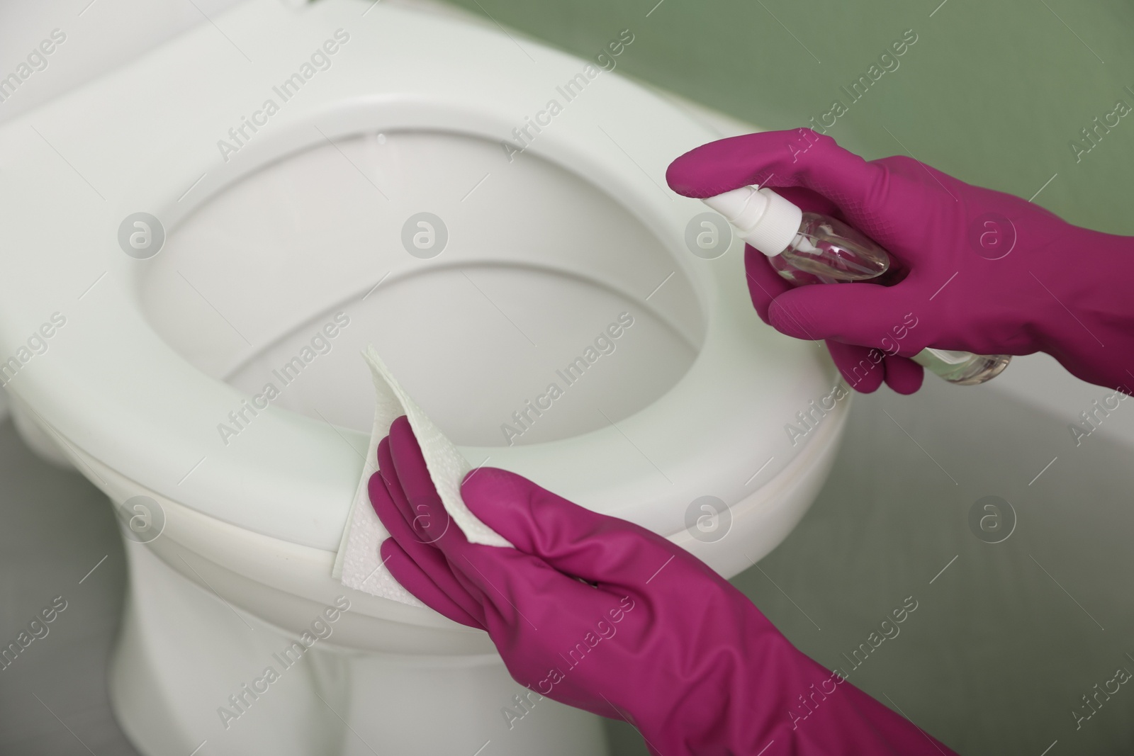 Photo of Woman disinfecting toilet seat in restroom, closeup