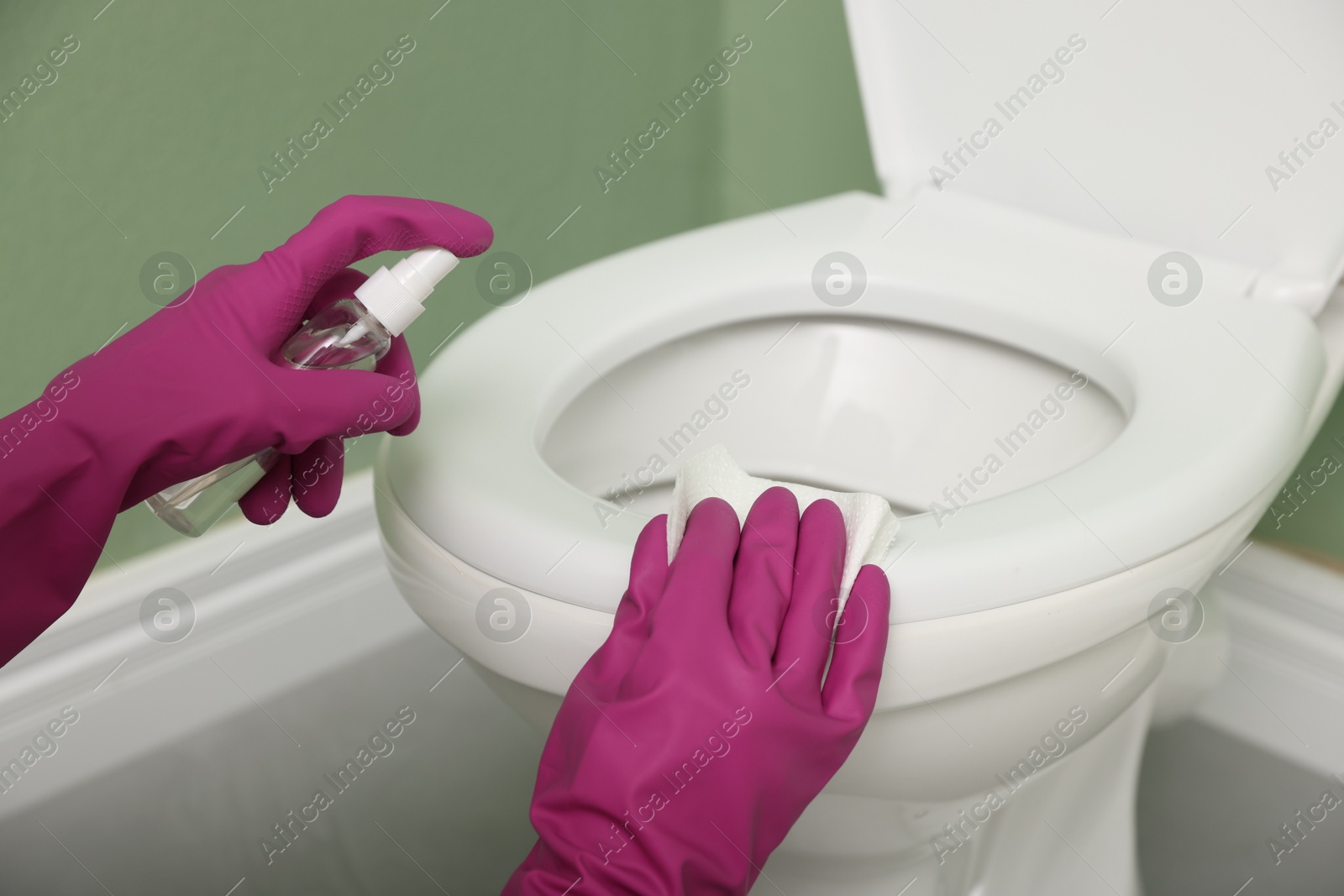 Photo of Woman disinfecting toilet seat in restroom, closeup