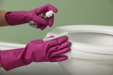 Photo of Woman disinfecting toilet seat in restroom, closeup