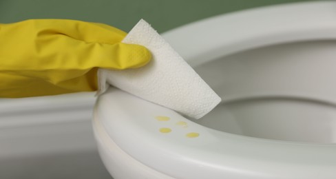 Photo of Woman wiping urine drops from toilet seat in restroom, closeup