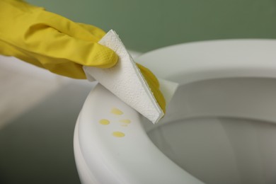 Photo of Woman wiping urine drops from toilet seat in restroom, closeup