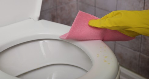 Photo of Woman wiping urine drops from toilet seat in restroom, closeup