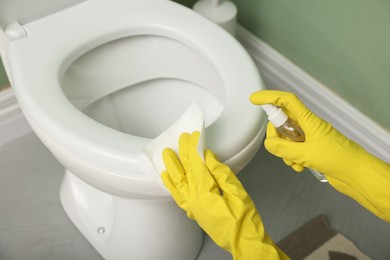 Photo of Woman disinfecting toilet seat in restroom, closeup