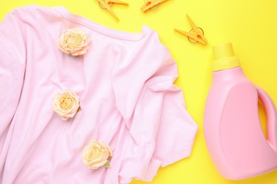 Photo of Bottle of laundry detergent, t-shirt, flowers and clothespins on yellow background, flat lay