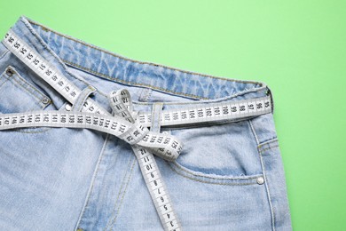 Jeans and measuring tape on green background, top view