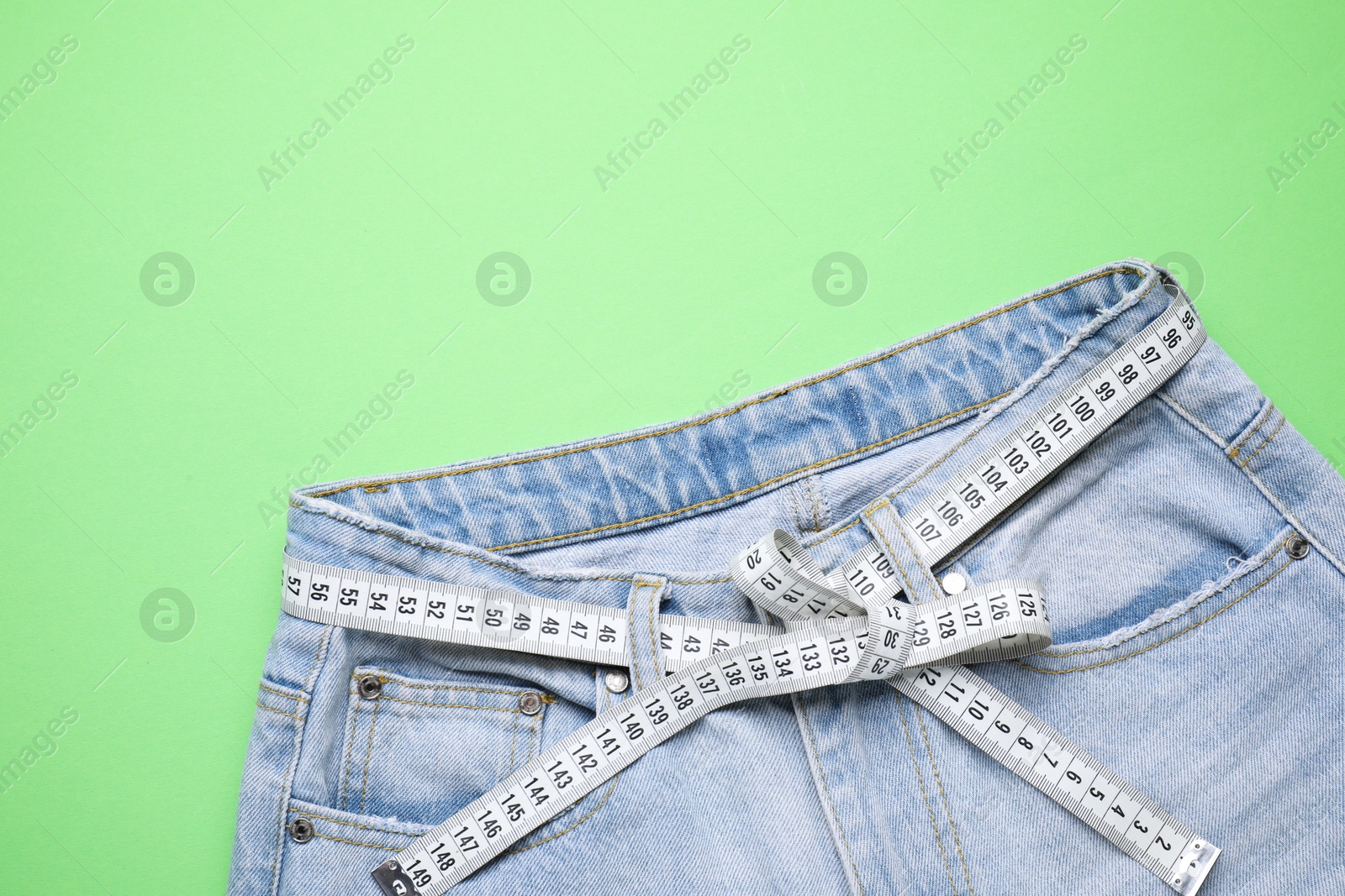 Photo of Jeans and measuring tape on green background, top view