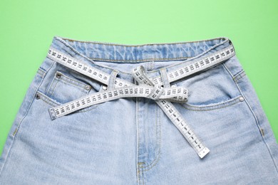 Photo of Jeans and measuring tape on green background, top view