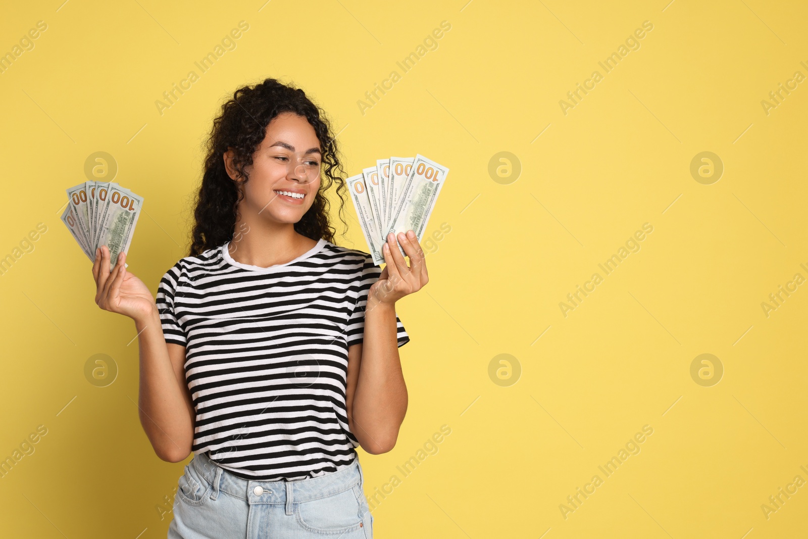 Photo of Happy woman with dollar banknotes on yellow background, space for text