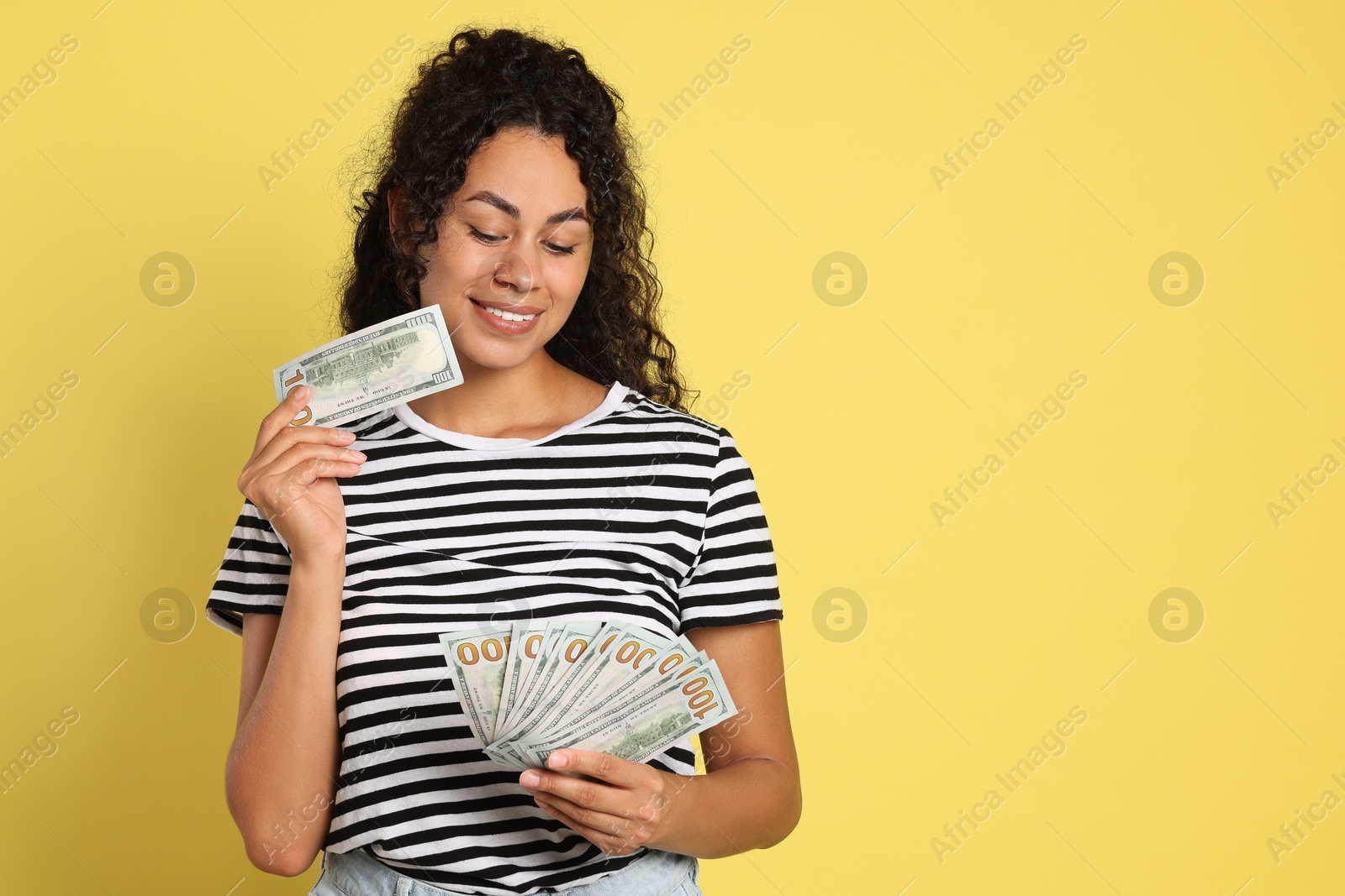 Photo of Happy woman with dollar banknotes on yellow background, space for text