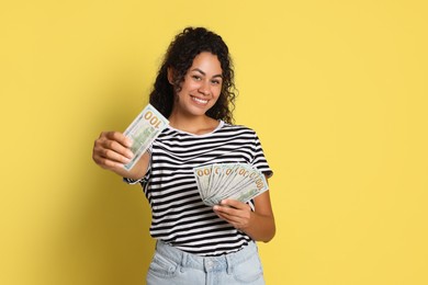 Happy woman with dollar banknotes on yellow background