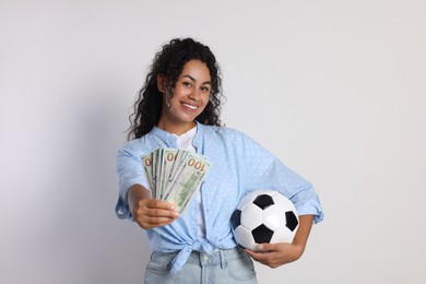 Happy woman with money and soccer ball on light grey background