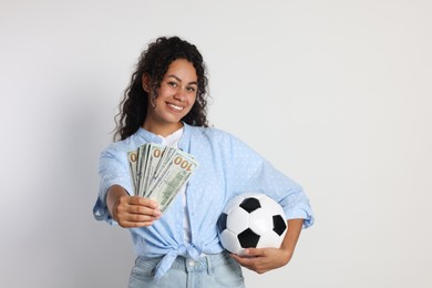 Happy woman with money and soccer ball on light grey background