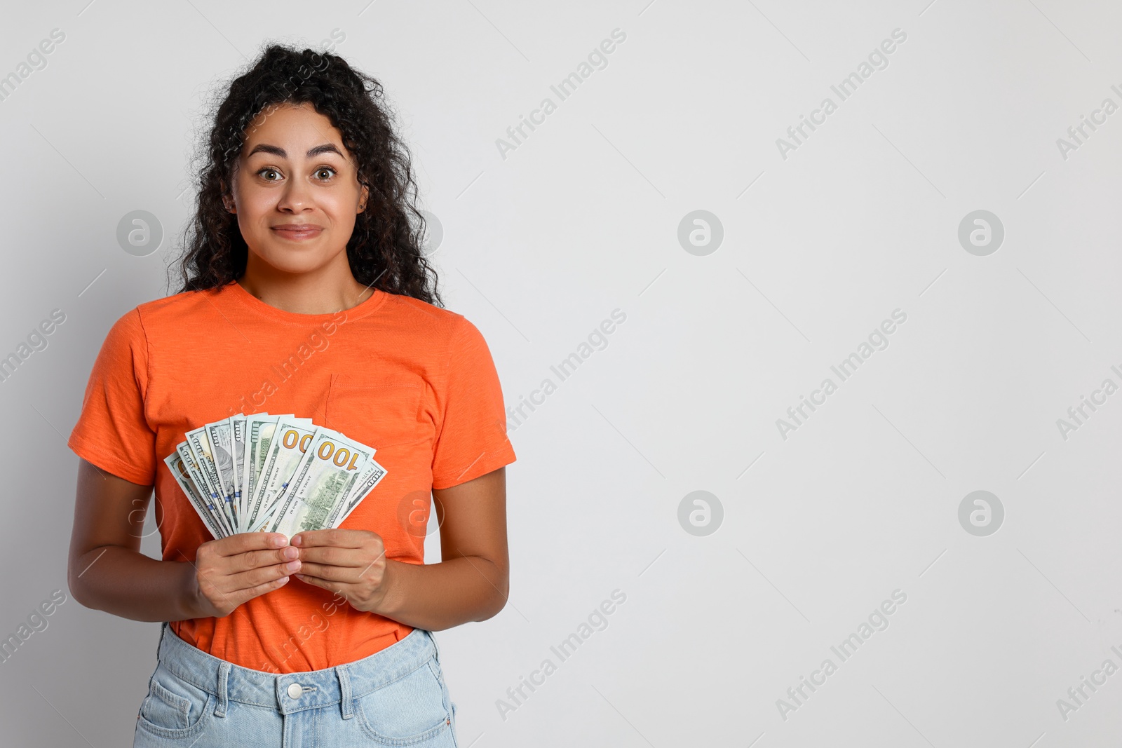 Photo of Smiling woman with dollar banknotes on light grey background, space for text