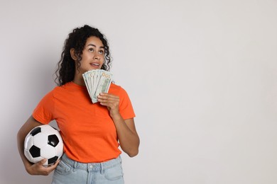 Happy woman with money and soccer ball on light grey background, space for text