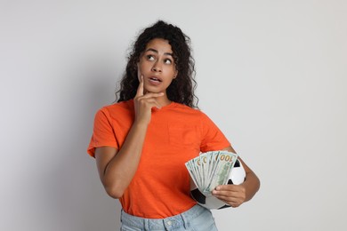 Woman with money and soccer ball on light grey background