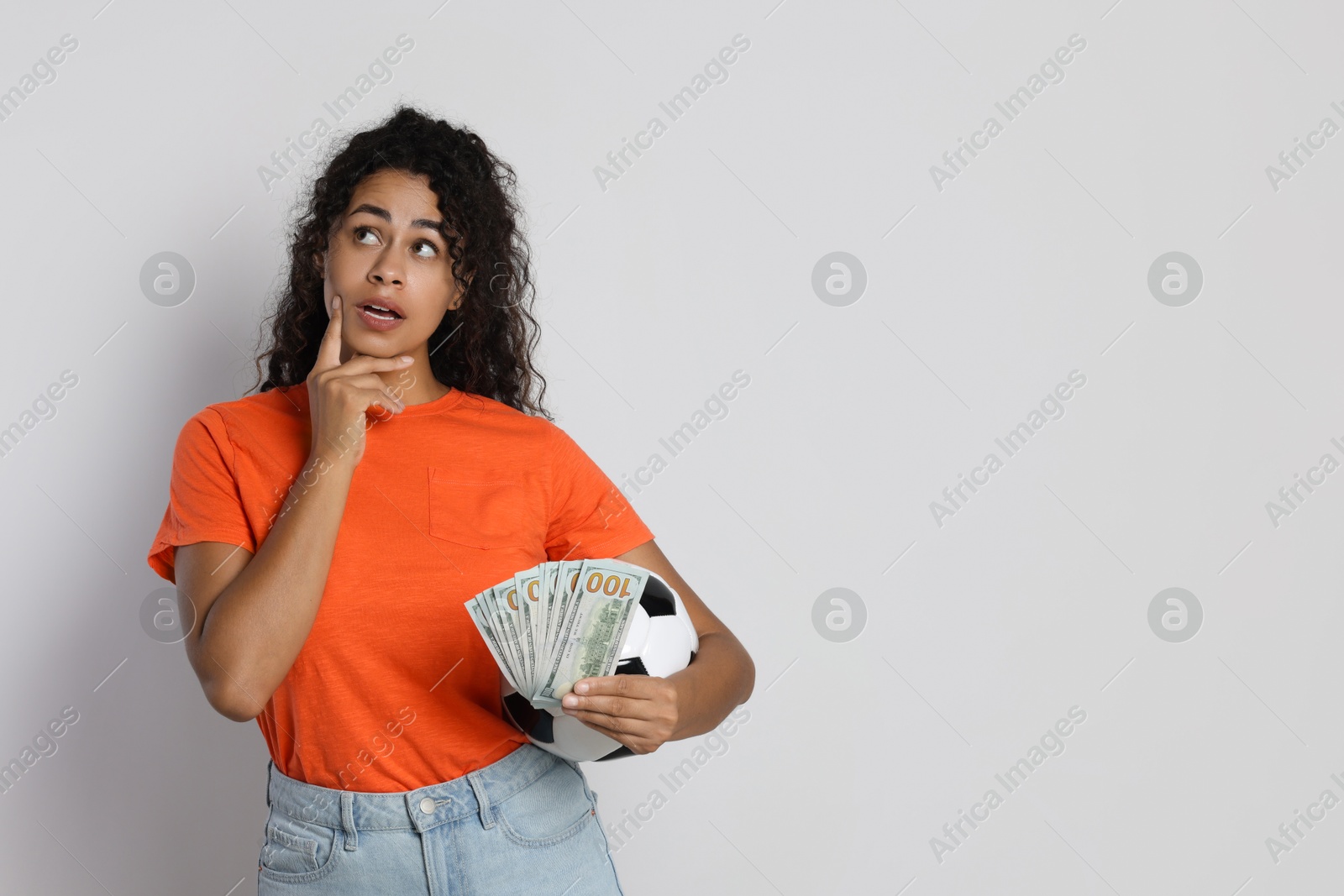 Photo of Woman with money and soccer ball on light grey background, space for text