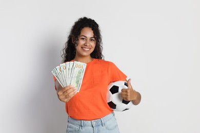 Happy woman with money and soccer ball on light grey background