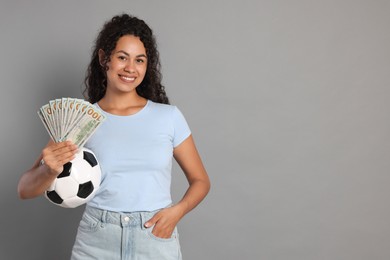 Photo of Happy woman with money and soccer ball on grey background, space for text