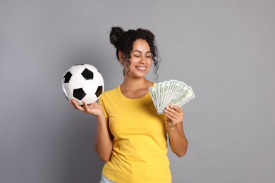 Happy woman with money and soccer ball on grey background