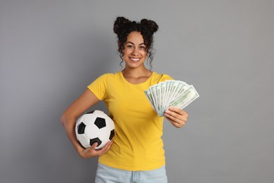 Happy woman with money and soccer ball on grey background