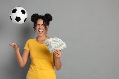 Happy woman with money throwing soccer ball on grey background, space for text