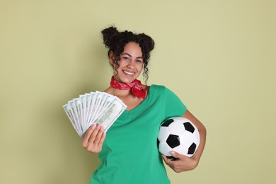 Happy woman with money and soccer ball on pale green background