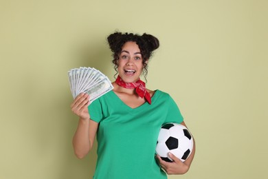 Happy woman with money and soccer ball on pale green background