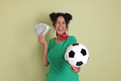 Happy woman with money and soccer ball on pale green background