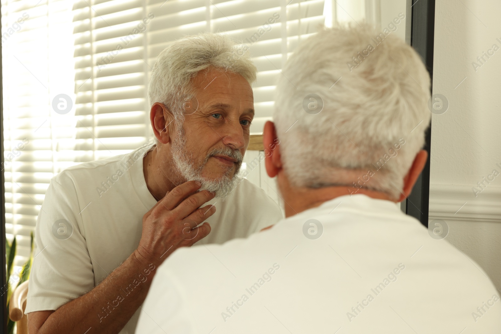 Photo of Senior man looking in mirror at home