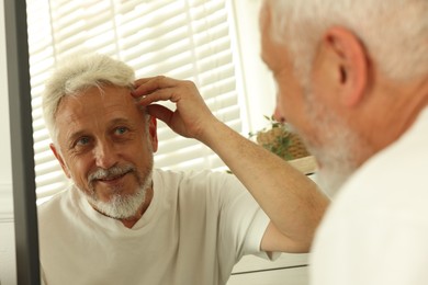 Photo of Senior man looking in mirror at home