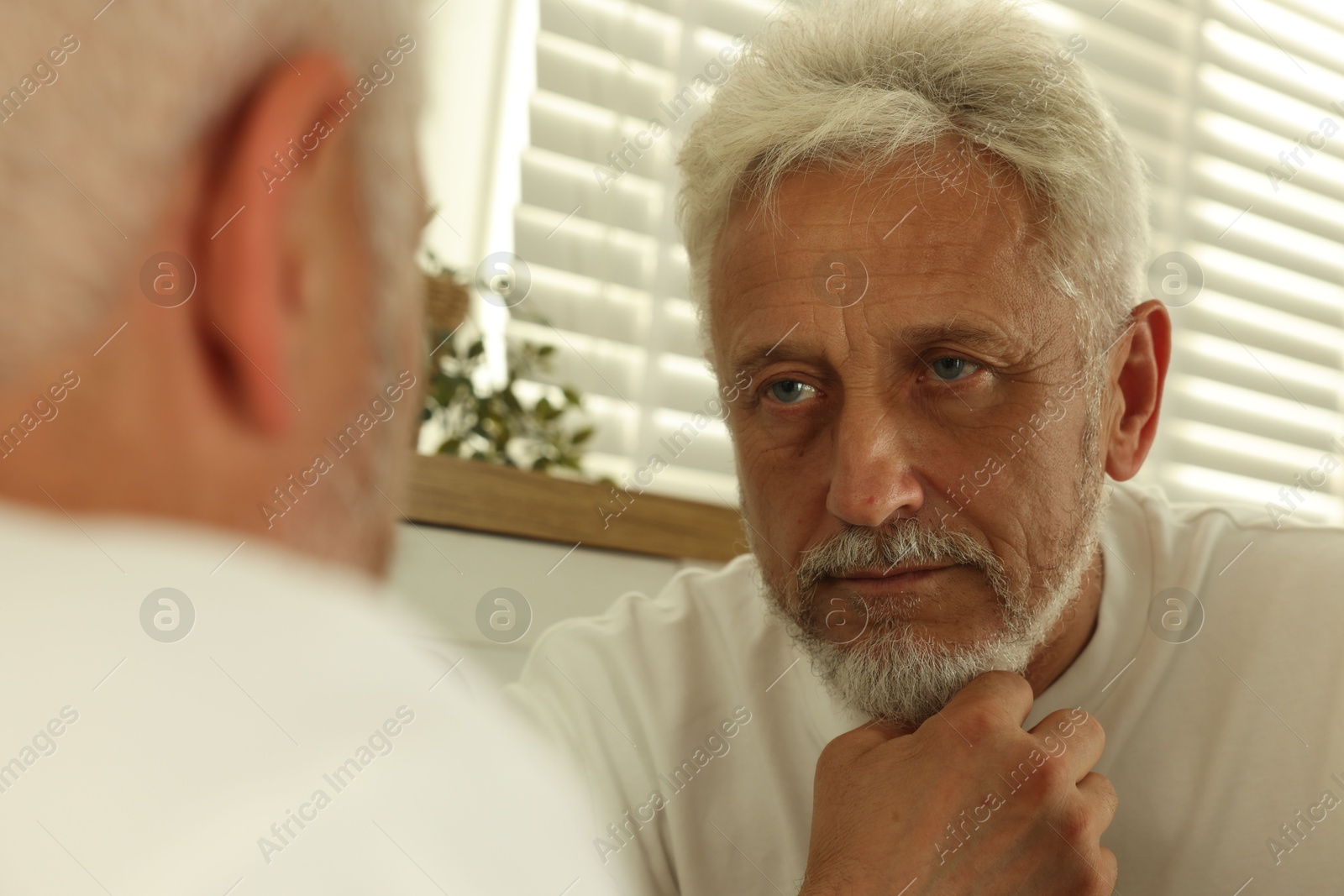 Photo of Senior man looking in mirror at home