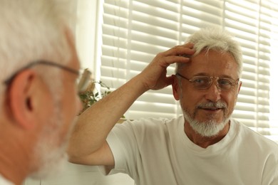 Photo of Senior man looking in mirror at home