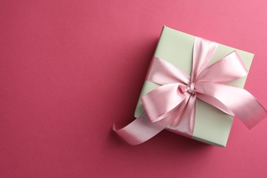 Beautiful gift box with bow on pink background, top view. Space for text