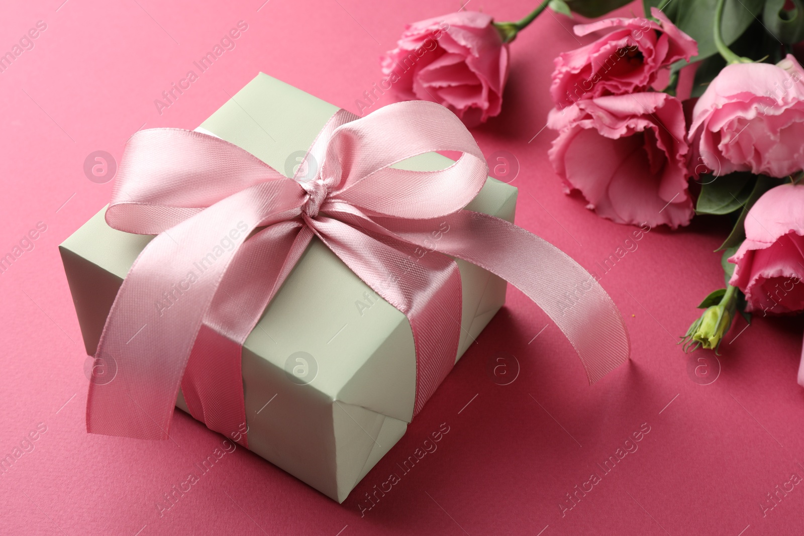 Photo of Beautiful gift box with bow and eustoma flowers on pink background, closeup