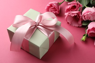 Photo of Beautiful gift box with bow and eustoma flowers on pink background, closeup