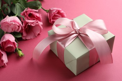 Photo of Beautiful gift box with bow and eustoma flowers on pink background, closeup