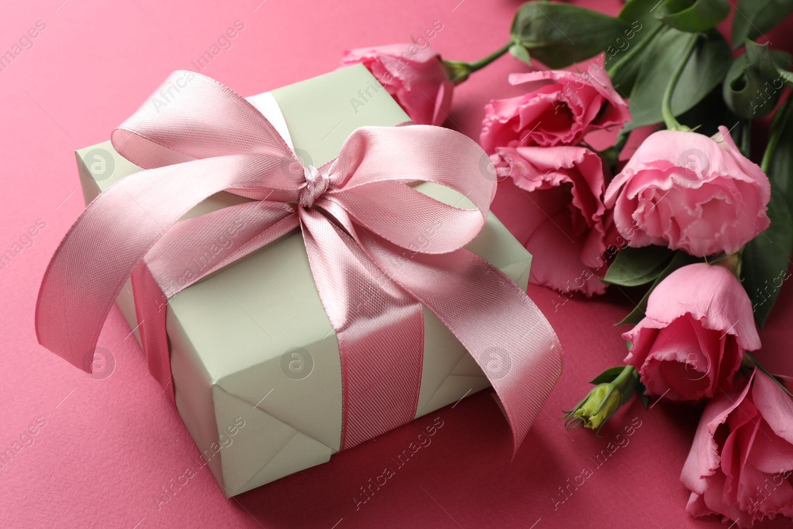 Photo of Beautiful gift box with bow and eustoma flowers on pink background, closeup