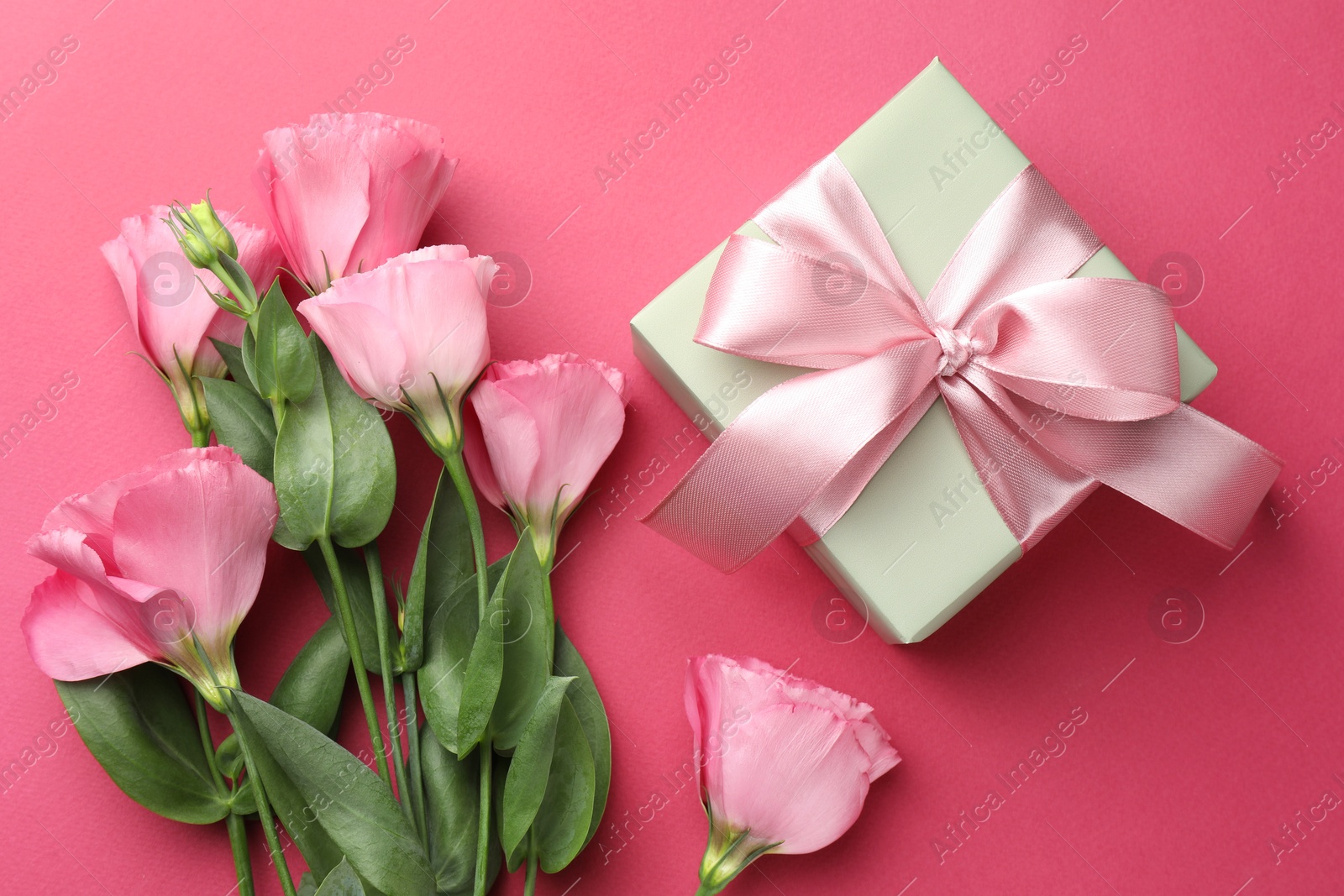 Photo of Beautiful gift box with bow and eustoma flowers on pink background, flat lay