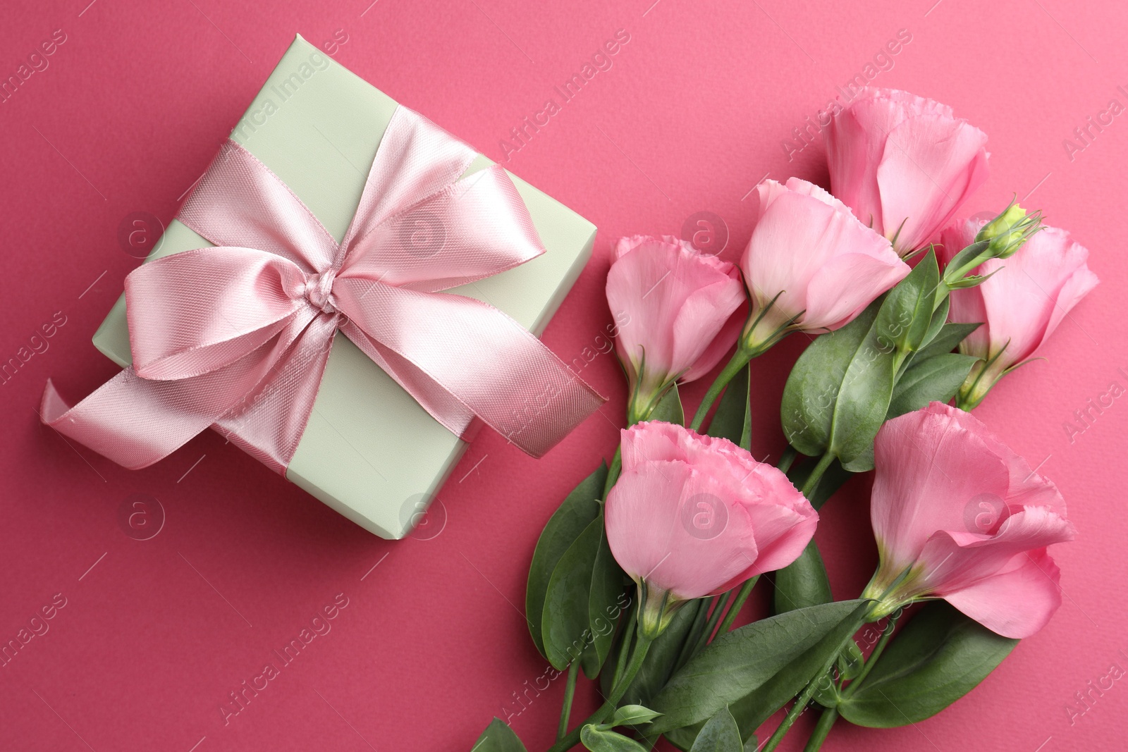 Photo of Beautiful gift box with bow and eustoma flowers on pink background, flat lay